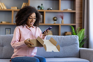 Excited woman looking at her new phone and holding the box it was delivered to her home in.