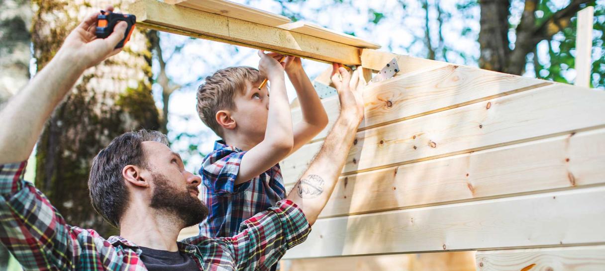 Father and son outdoors, measuring wood soon to be cut for a wood working project.